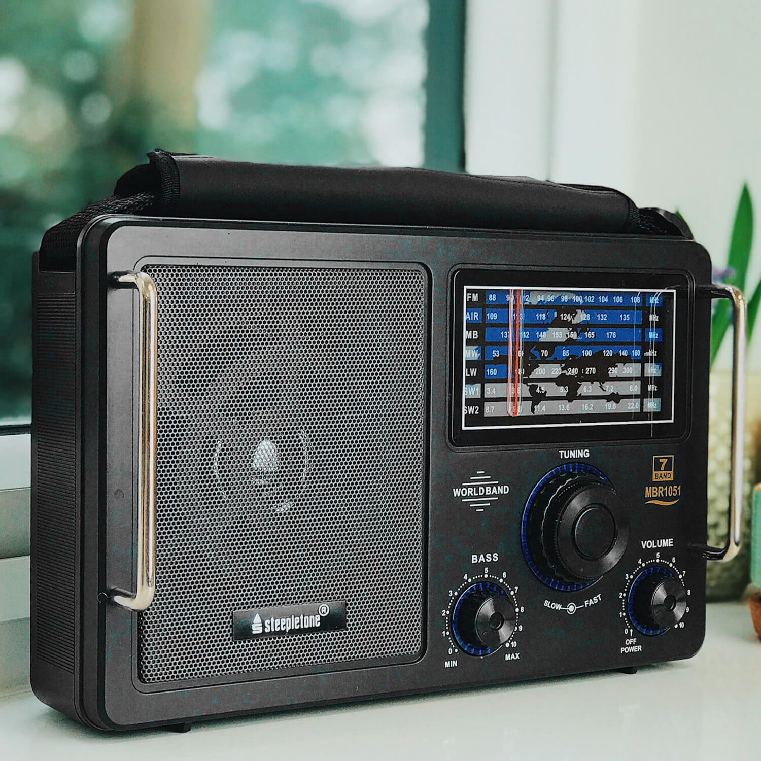 A black radio on a window sill with green foliage behind.